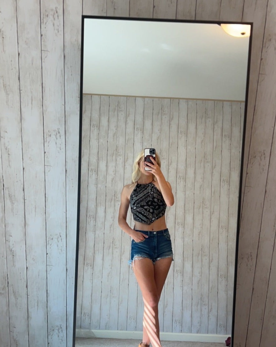 A model wearing a boho bandana crop top and denim shorts in front of a mirror.