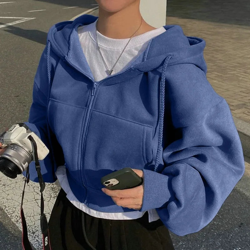 Cropped slim fit smooth silhouette zip-up sweatshirt in blue worn by a person holding a camera.