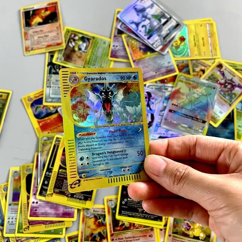 A hand holding a Gyarados card from the 54pcs Pokémon MEGA card set with other cards in the background.