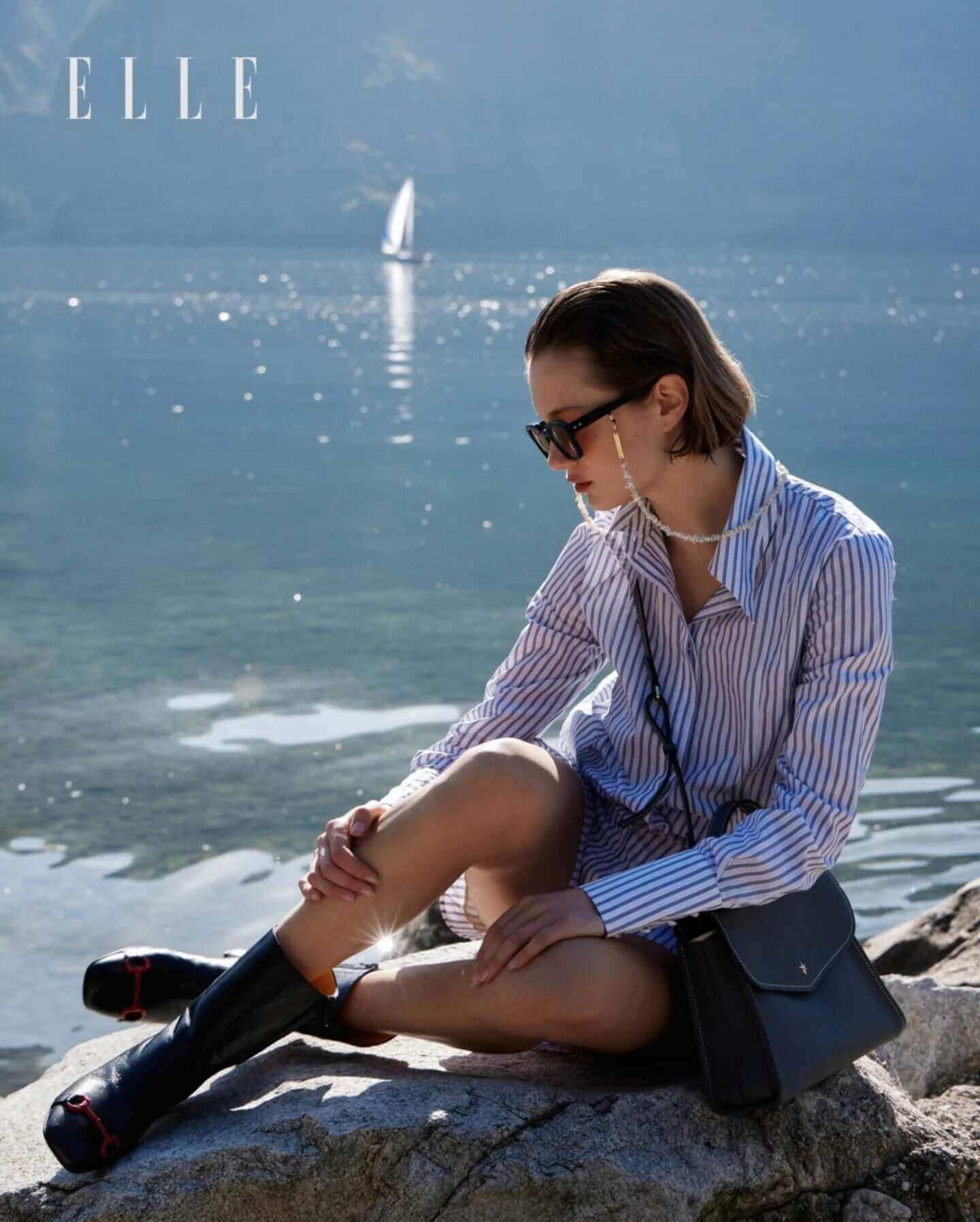 Model showcasing black leather back stripe boots by the water while wearing a stylish striped shirt.